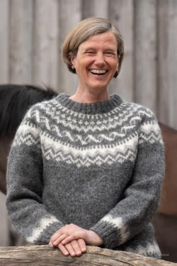 Silke Möller, Feldenkrais-Pädagogin für Mensch und Pferd, lächelt freundlich vor einer Holzwand im grauen Islandpullover.